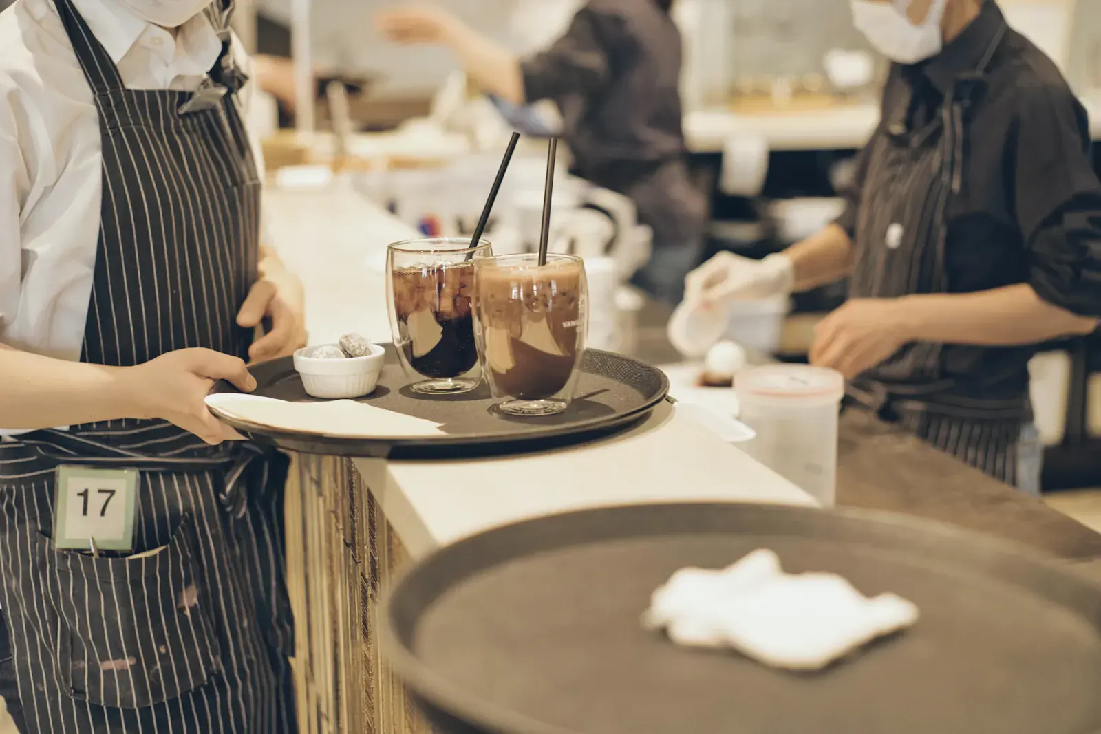 Servers in aprons carry trays through a dining room